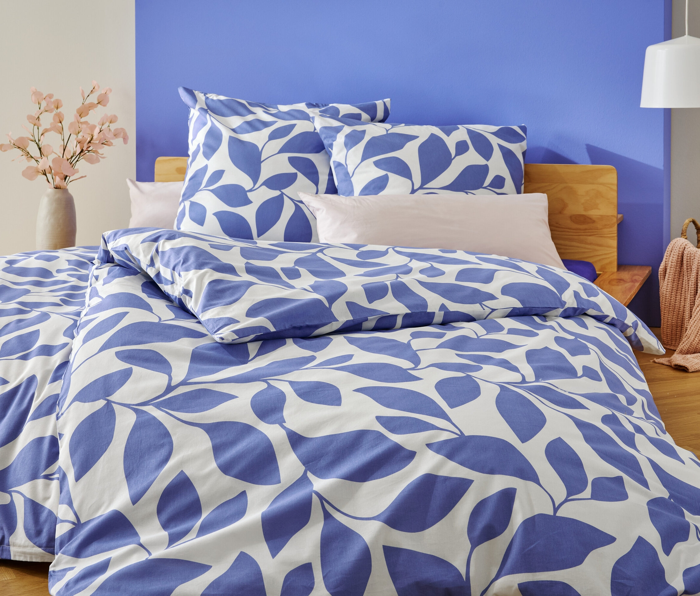 Un lit avec une literie à feuilles bleues et blanches se trouve devant un mur peint en bleu et blanc.