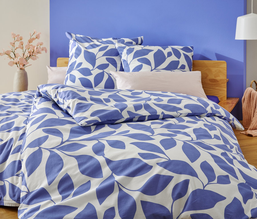 Un lit avec une literie à feuilles bleues et blanches se trouve devant un mur peint en bleu et blanc.