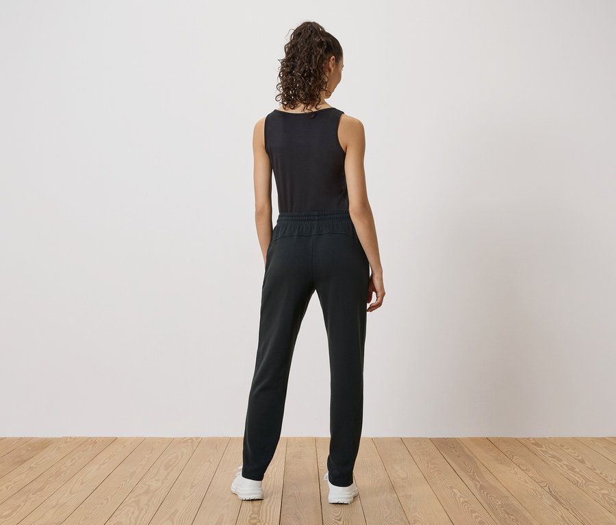 Vue arrière d'une femme aux cheveux bouclés portant un débardeur noir, un pantalon noir et des baskets blanches.