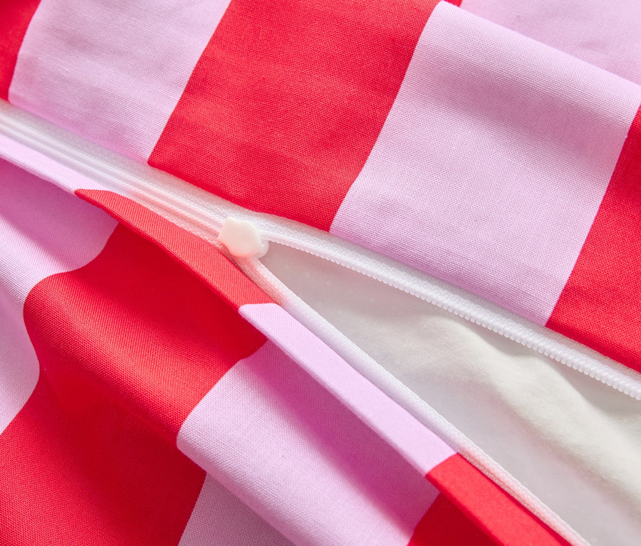 Gros plan d'une housse de couette partiellement ouverte avec des rayures rouge et rose et une fermeture éclair blanche.