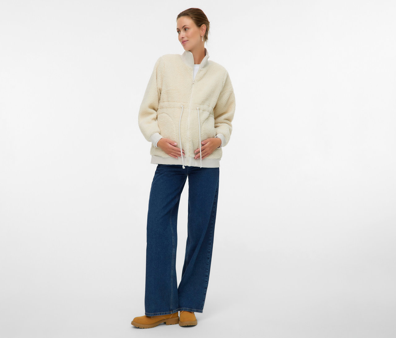 Une femme enceinte porte la veste Teddy 3 en 1 MAMALICIOUS «
MLCARLY » sur un jean et des bottines.