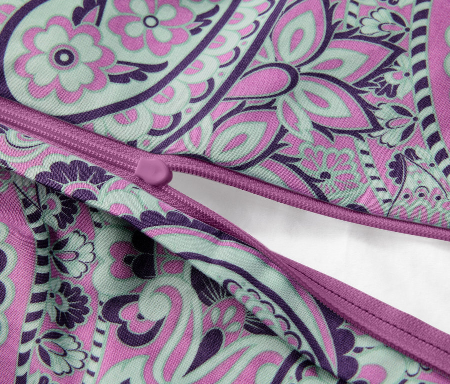 Gros plan d'un coussin partiellement ouvert avec une fermeture éclair et un motif floral violet, rose et vert.