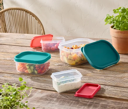 Plusieurs récipients de stockage transparents avec des couvercles colorés sont posés sur une table en bois.