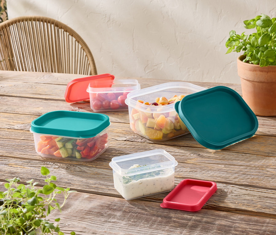 Plusieurs récipients de stockage transparents avec des couvercles colorés sont posés sur une table en bois.
