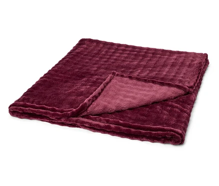 Une couverture moelleuse bordeaux pliée avec une texture côtelée, posée sur un fond blanc. Un coin est replié.