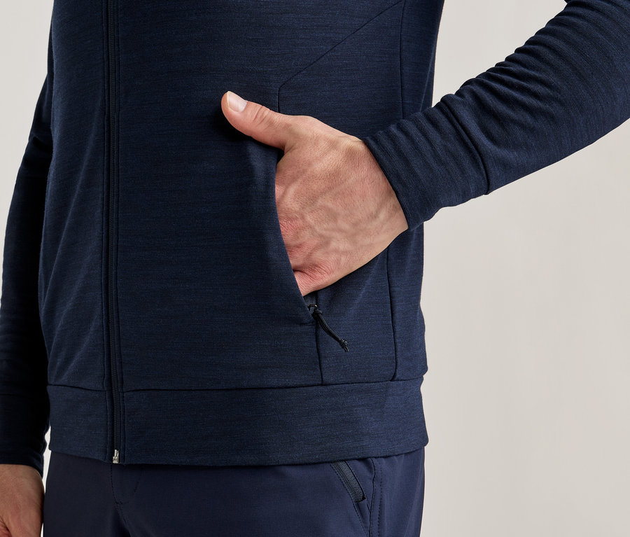Gros plan d'une personne portant une veste zippée bleu marine avec une main dans la poche.