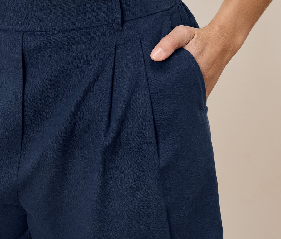Gros plan d'une personne portant un pantalon bleu marine à plis avec une main dans la poche.