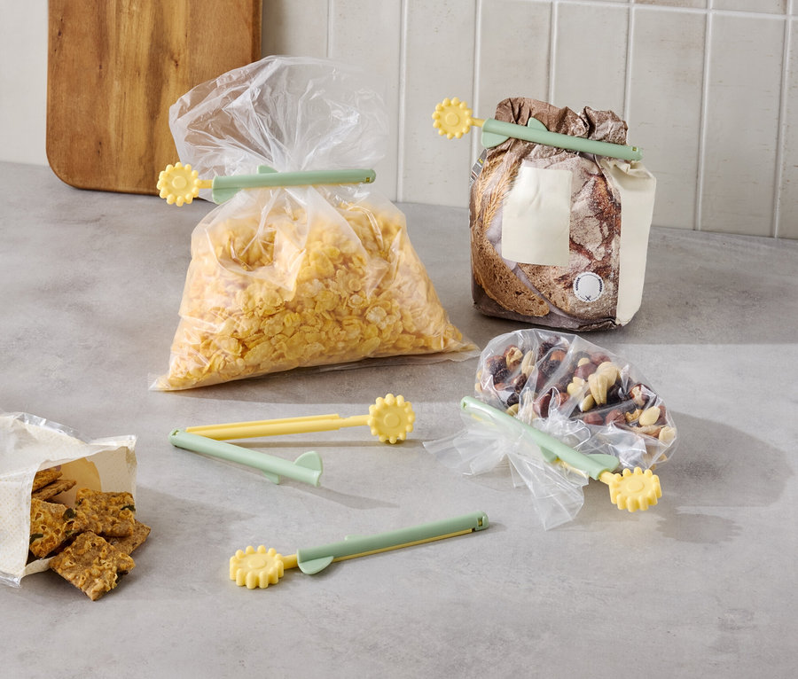 Divers aliments sont emballés dans des sacs avec des clips de fermeture jaune-vert sur un comptoir de cuisine.