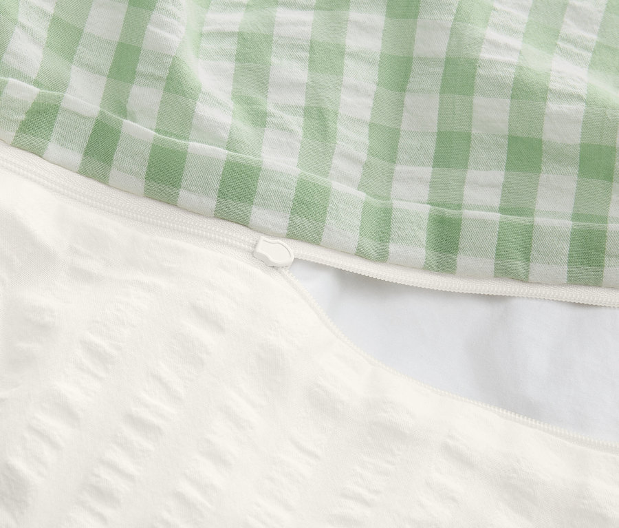 Gros plan d'une housse de couette partiellement ouverte avec fermeture éclair, dessus à carreaux verts et blancs, dessous blanc texturé.
