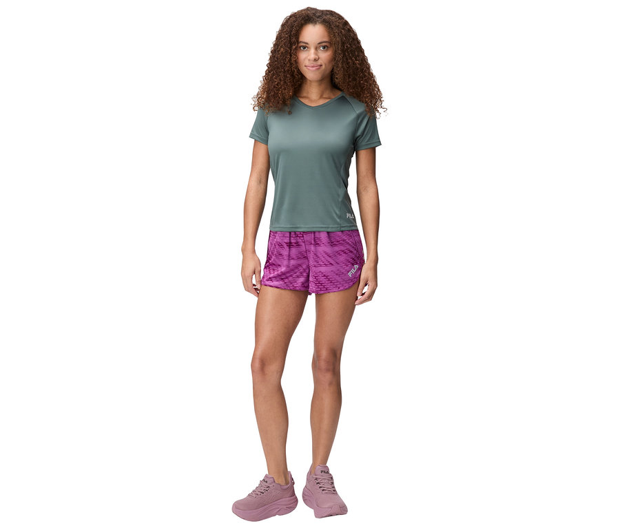 Femme debout avec un t-shirt gris-bleu, un short violet et des chaussures lilas.