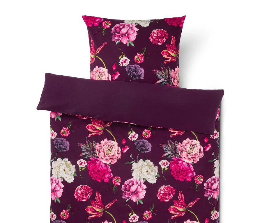 Parure de lit violet foncé à motif floral, comprenant un oreiller et une housse de couette pliée avec des pivoines roses, fuchsia et blanches.