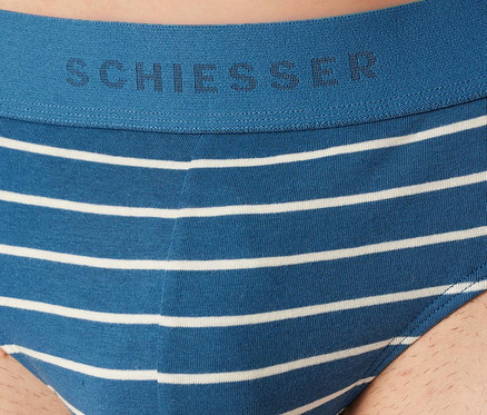 Un homme porte un slip SCHIESSER Rio bleu à rayures blanches. La ceinture bleue porte le logo SCHIESSER.