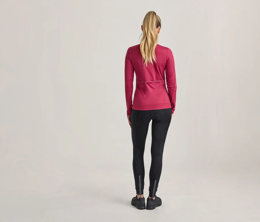 Femme vue de dos, portant un haut de sport rose à manches longues, un legging noir avec des bandes réfléchissantes et des chaussures de sport noires.