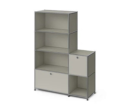 Une étagère modulaire en forme de L, gris clair avec des cadres chromés. La section gauche plus haute a deux étagères ouvertes avec des côtés perforés, une étagère ouverte avec des côtés pleins et un meuble fermé avec une poignée. La section droite plus courte a un meuble fermé avec une poignée et une étagère ouverte en dessous.
