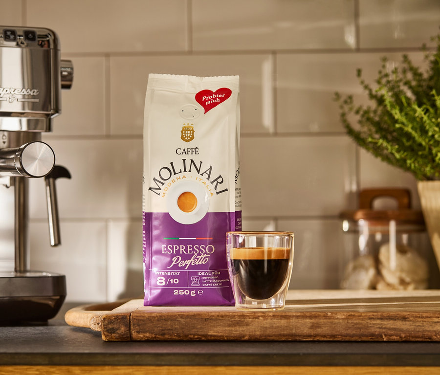 Une machine à porte-filtre « Lapressa » argentée, un paquet de Caffè Molinari et une tasse d'espresso sur une planche en bois.