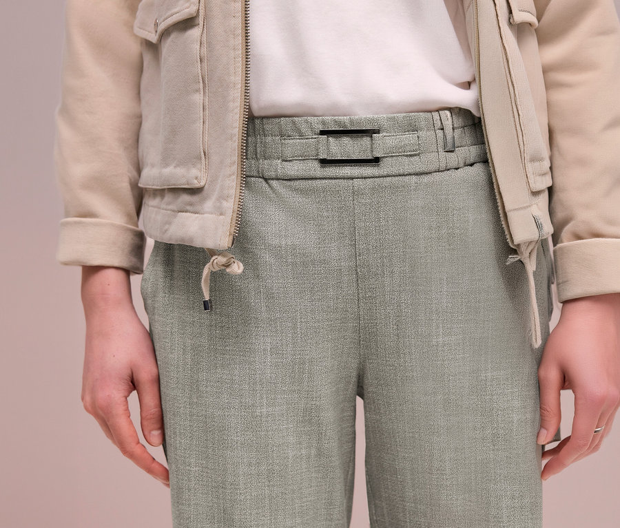 Personne portant une veste beige sur un t-shirt blanc et un pantalon de jogging Street One vert clair avec une boucle noire à la taille.