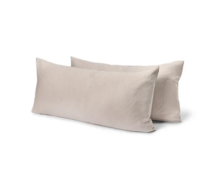 Deux oreillers rectangulaires beige clair, l'un légèrement derrière l'autre, sur un fond blanc.