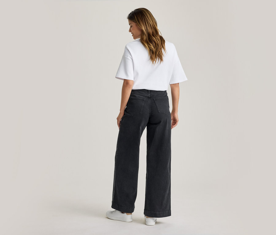 Femme vue de dos portant un t-shirt blanc, un jean large foncé et des baskets blanches, regardant légèrement vers la gauche.