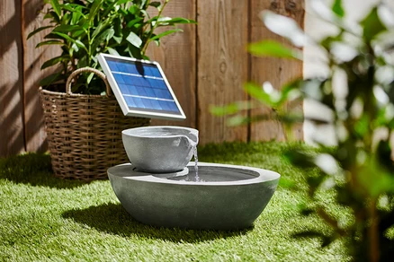 Fontaine solaire de jardin grise à deux vasques sur l'herbe.