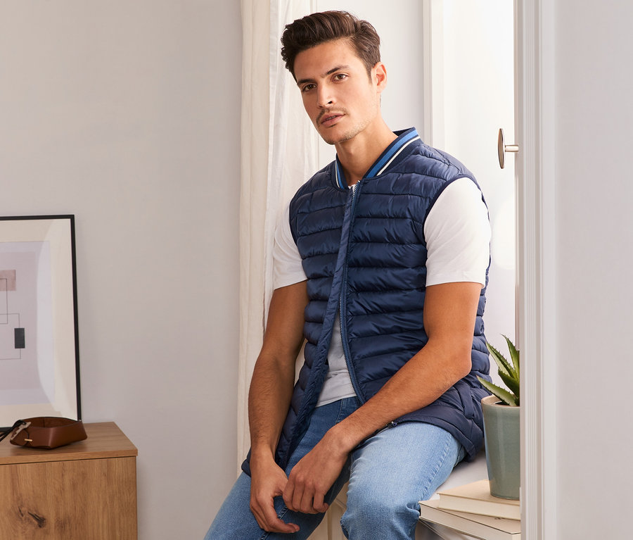 Un homme est assis sur un rebord de fenêtre et porte un gilet surpiqué bleu.