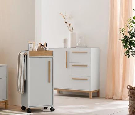 Salle de bain gris clair avec armoire haute Eklund, meuble sous-vasque avec tiroirs et meuble d'appoint. Avec serviettes beige et blanc rayé, tapis de douche et paniers de rangement.