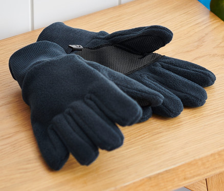 Des gants en polaire pour enfants sont posés sur un banc en bois à côté d'un sac à dos et d'un skateboard.