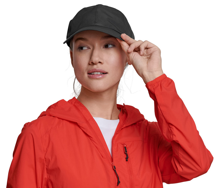 Femme touchant la visière d'une casquette pour tous temps noire. Elle porte une veste rouge.