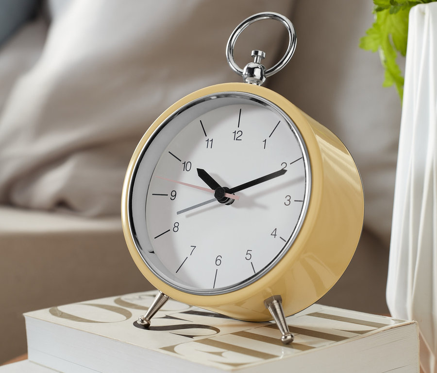 Un réveil analogique rétro jaune posé sur deux livres blancs.