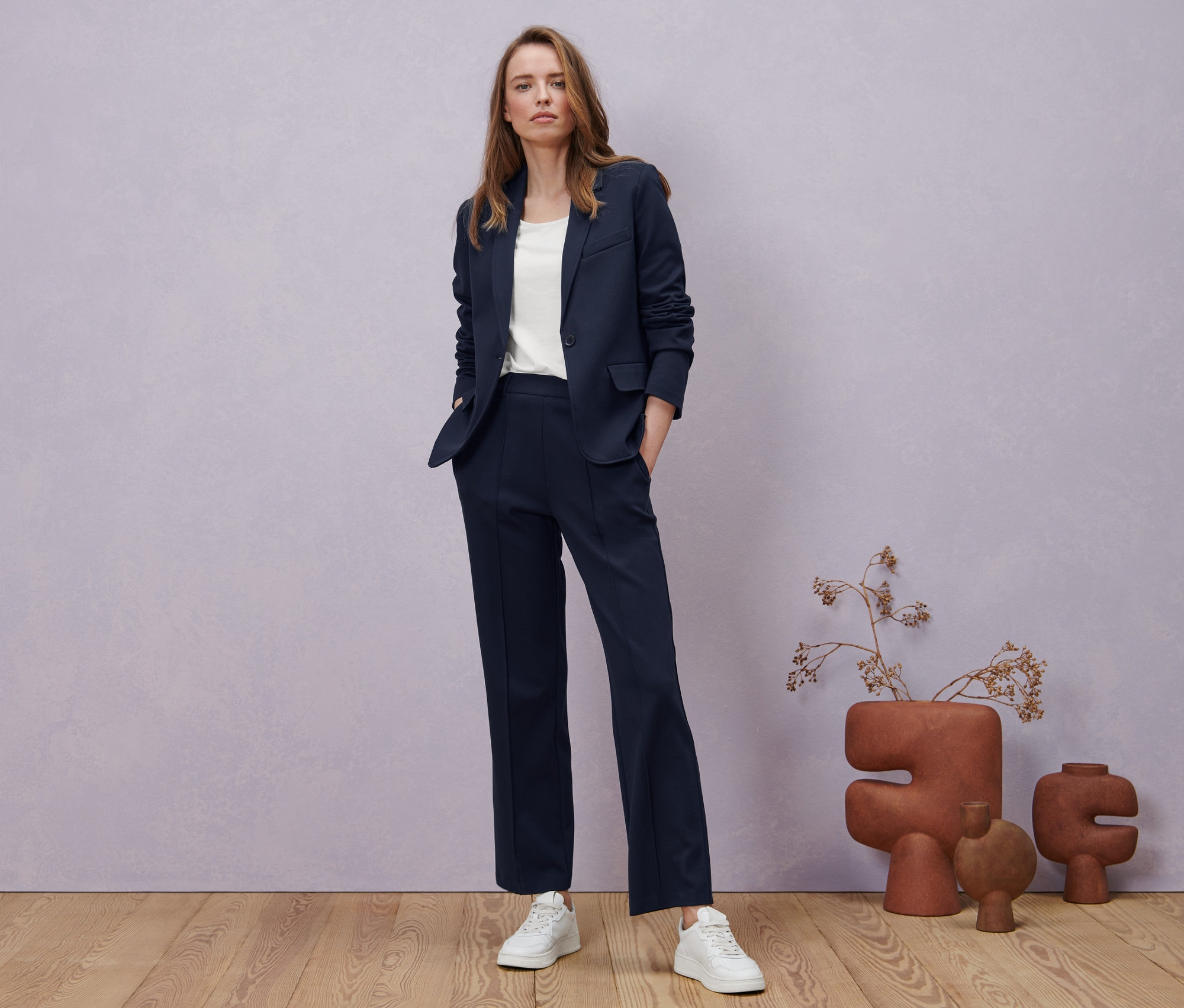 Une femme pose en pantalon en jersey avec nervure bleu foncé, un blazer en jersey et un t-shirt demi-manches, blanc.