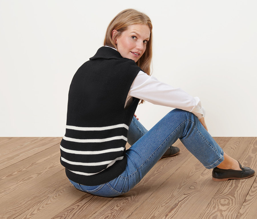 Femme assise par terre portant un sous-pull à col camionneur noir avec des rayures blanches.