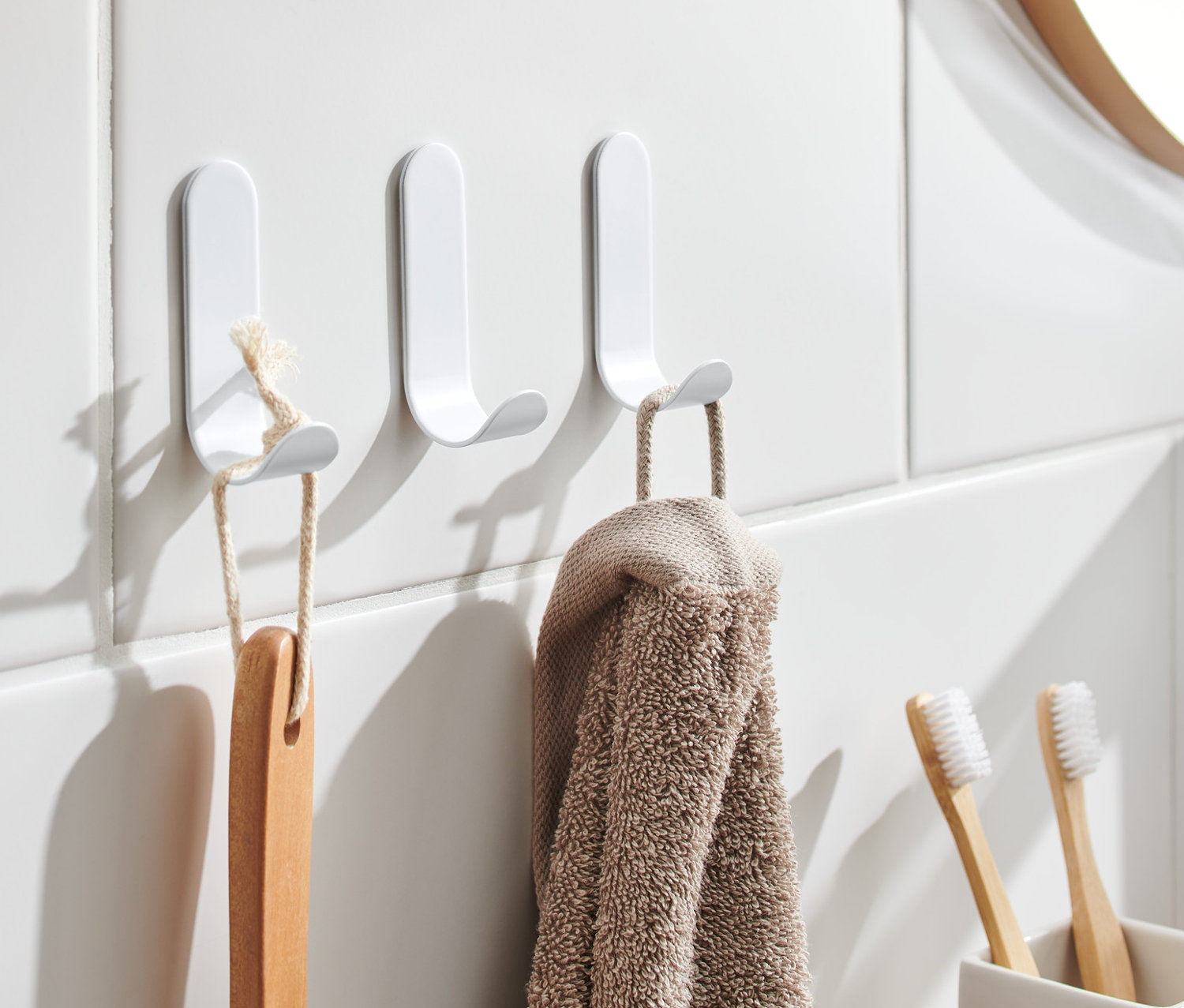 Trois crochets autocollants sont fixés sur des carreaux blancs, avec une brosse et une serviette suspendues.