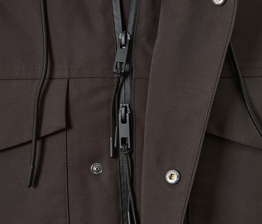 Gros plan sur une parka marron avec une fermeture éclair noire et des boutons-pression argentés.