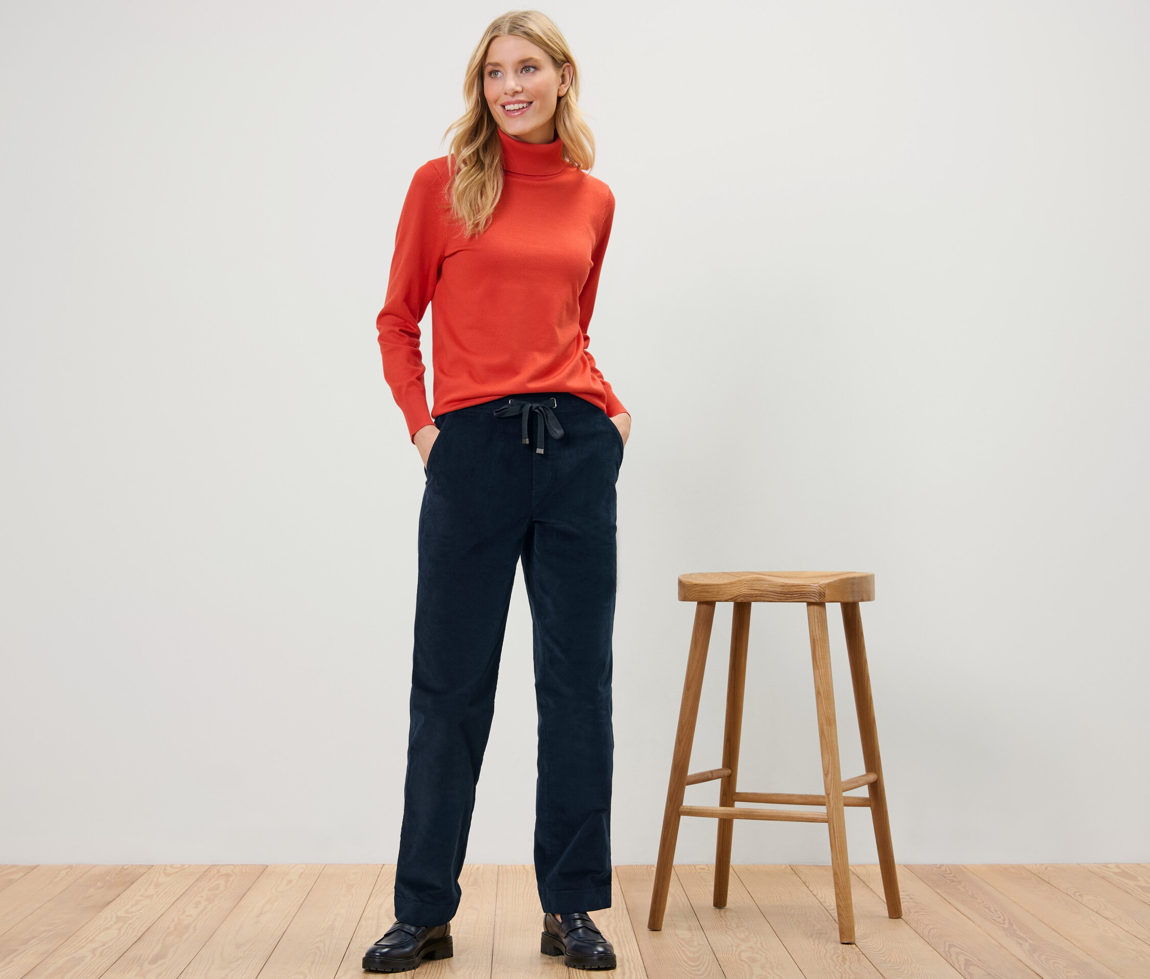 Femme posant en pantalon de jogging en velours côtelé et col roulé orange.