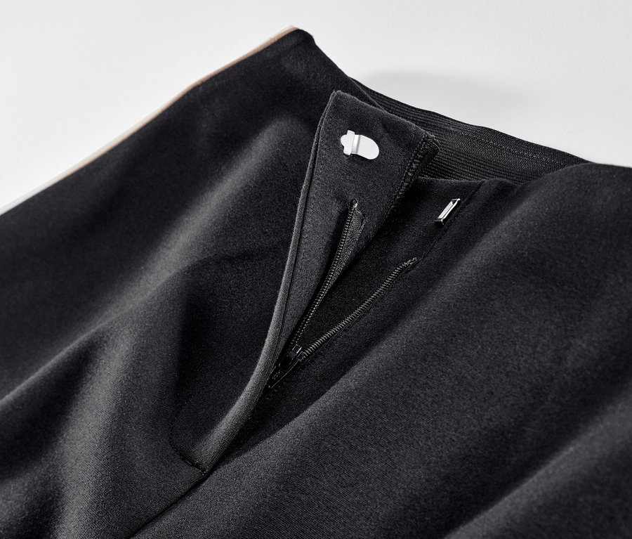 Gros plan sur un pantalon en jersey noir avec des bandes de galons et une fermeture éclair ouverte.