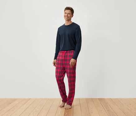 Un homme debout portant un haut bleu à manches longues et un pantalon de pyjama à carreaux rouges.
