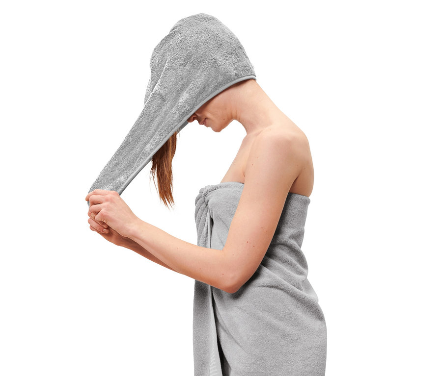 Une femme met une serviette turban sur sa tête, le corps enveloppé dans une serviette.