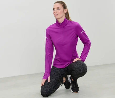 Une femme portant un t-shirt technique thermique rose baie fluo accroupie sur le sol.