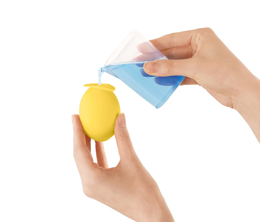 Une femme verse du liquide bleu d'une tasse à mesurer dans un embout anti-calcaire jaune pour robinet.