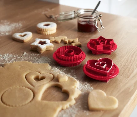 Sur une table en bois sont posés des sablés Linzer et 3 emporte-pièces pour sablés Linzer.