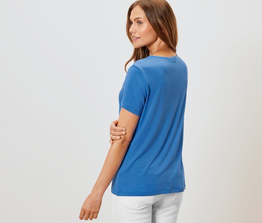 Femme posant en t-shirt avec soufflet bleu cobalt et pantalon blanc.