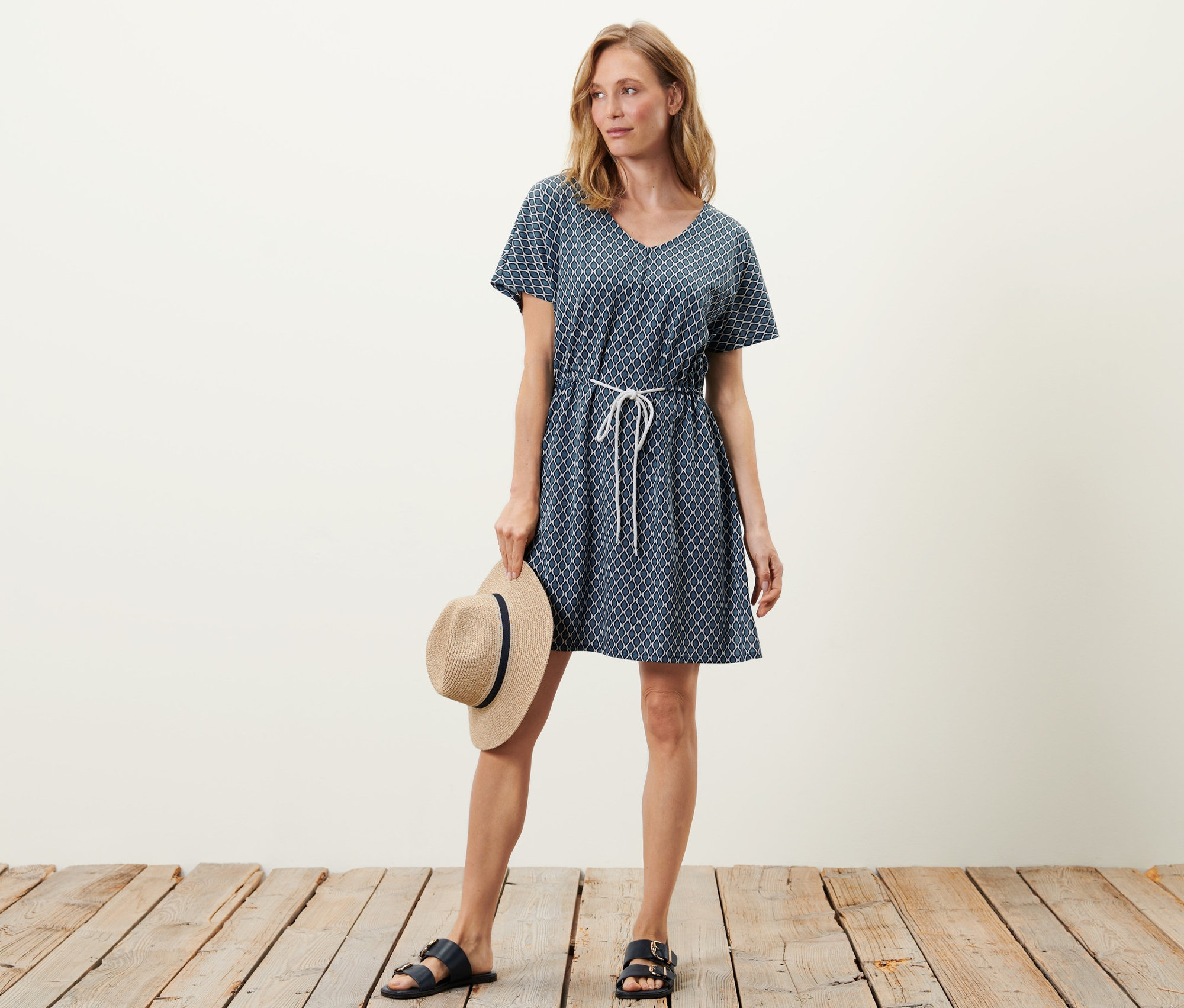 Femme posant en tunique de plage et tenant un chapeau.