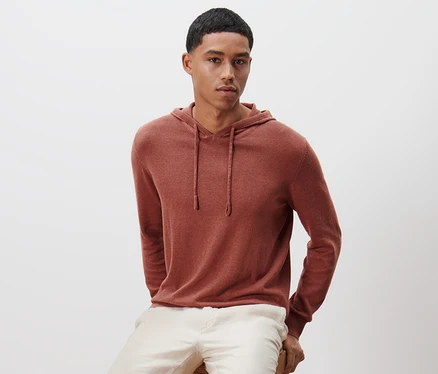Un homme est assis sur un tabouret en bois et porte un sweat-shirt à capuche en maille.