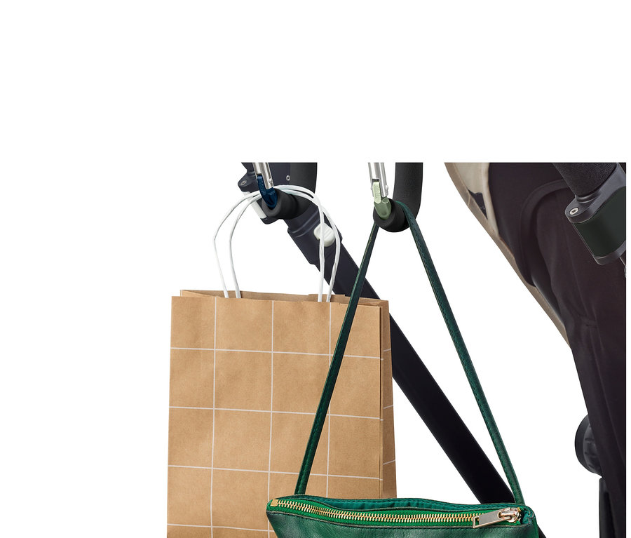 Un sac de courses et un sac à main vert sont suspendus à une poussette à l'aide de 2 mousquetons XXL.