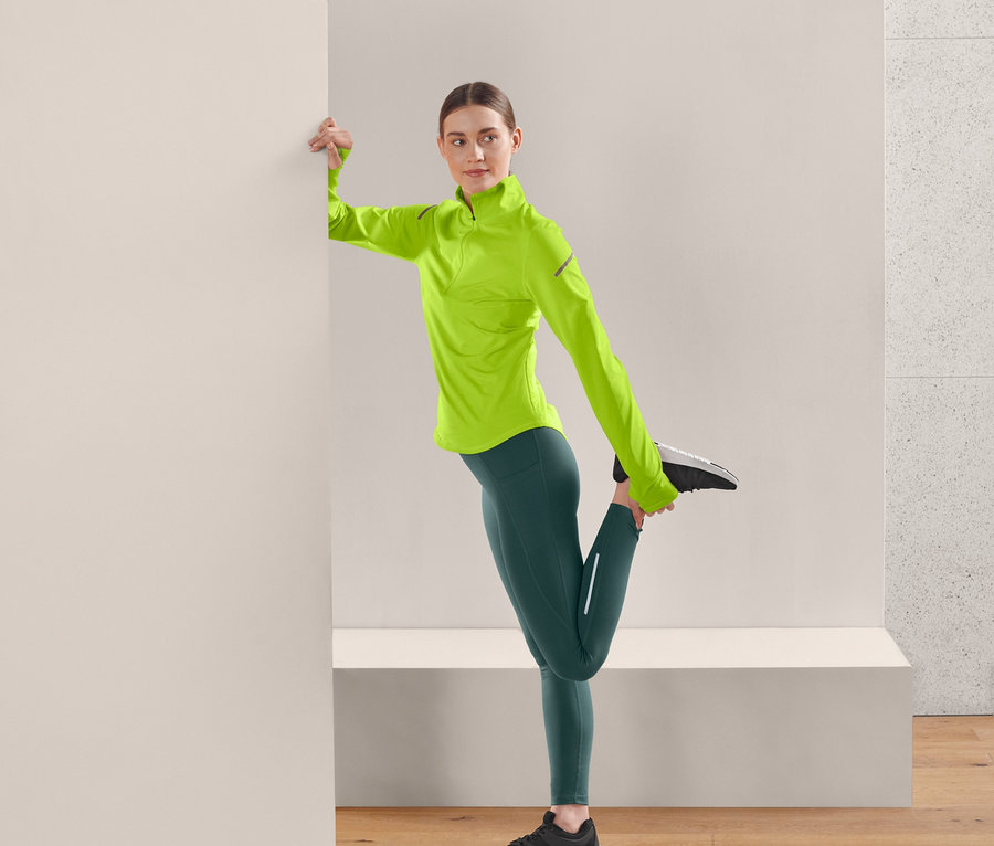 Femme étire sa jambe en portant un legging thermique de course vert foncé.