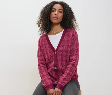 Une femme est assise et porte un cardigan en grosse maille à jacquard pied-de-poule.