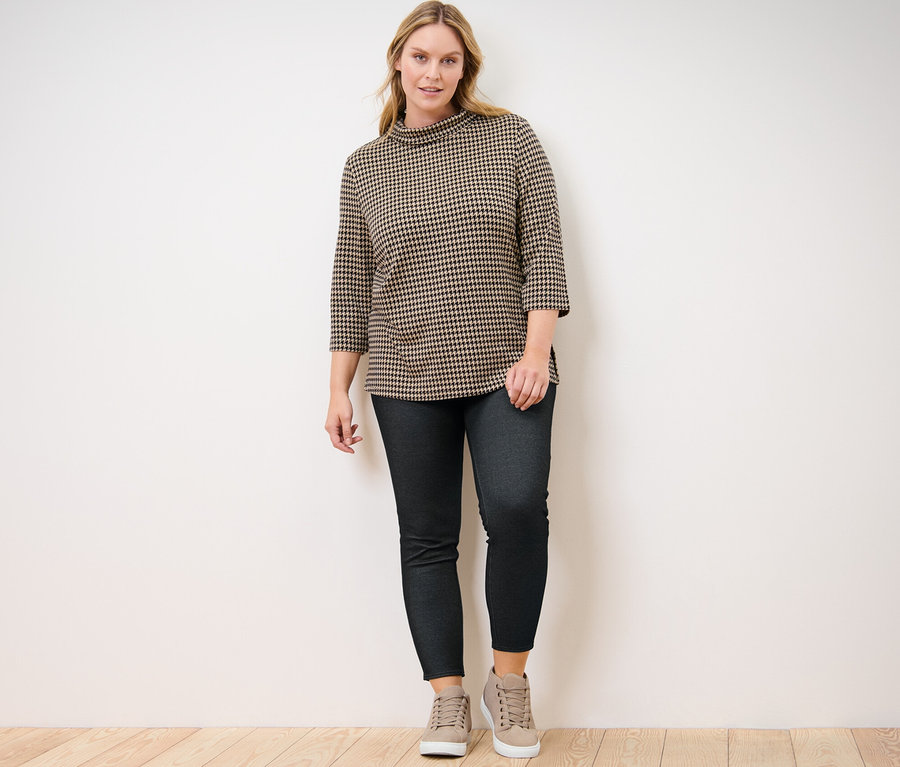 Une femme pose en legging doublé à l’aspect jean et en sweatshirt manches 3/4 pied de poule.