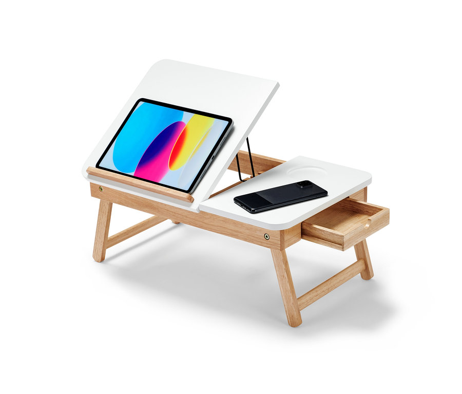 Une table de lit pour ordinateur portable avec un plateau blanc et des pieds en bois marron clair. Une tablette et un téléphone portable sont posés sur le plateau.