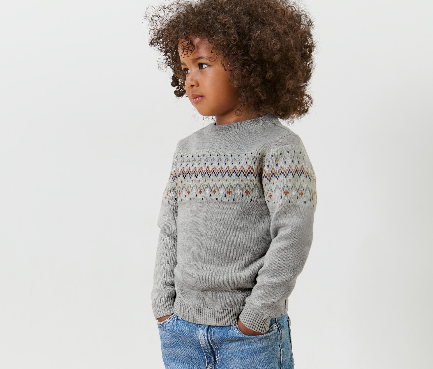 Vue latérale d'un enfant aux cheveux bouclés portant un pull en maille pour enfant gris et un jean.