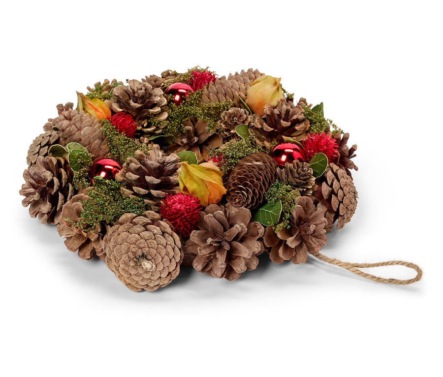 Couronne de pommes de pin avec des ornements rouges, des feuilles et des fleurs.