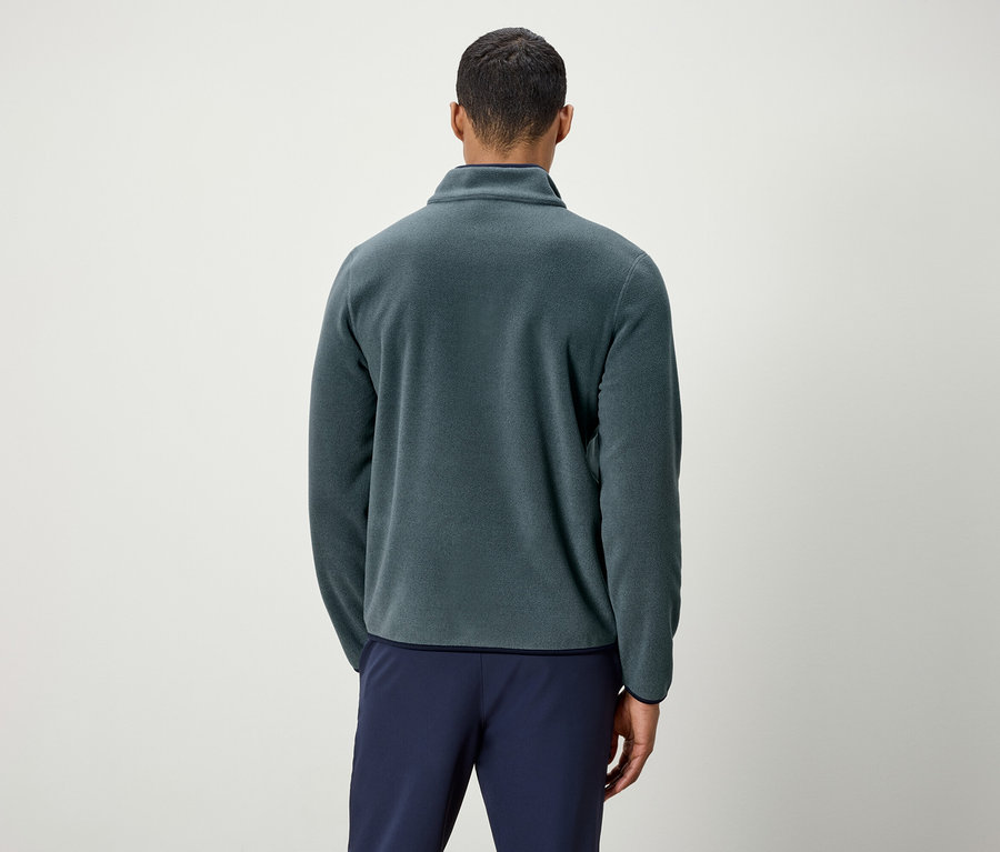 Un homme vu de dos portant une veste en polaire verte et un pantalon bleu.